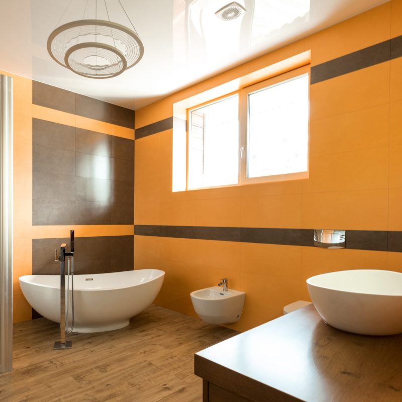 interior of bathroom in orange and white colors with bathtube, sink and bidet